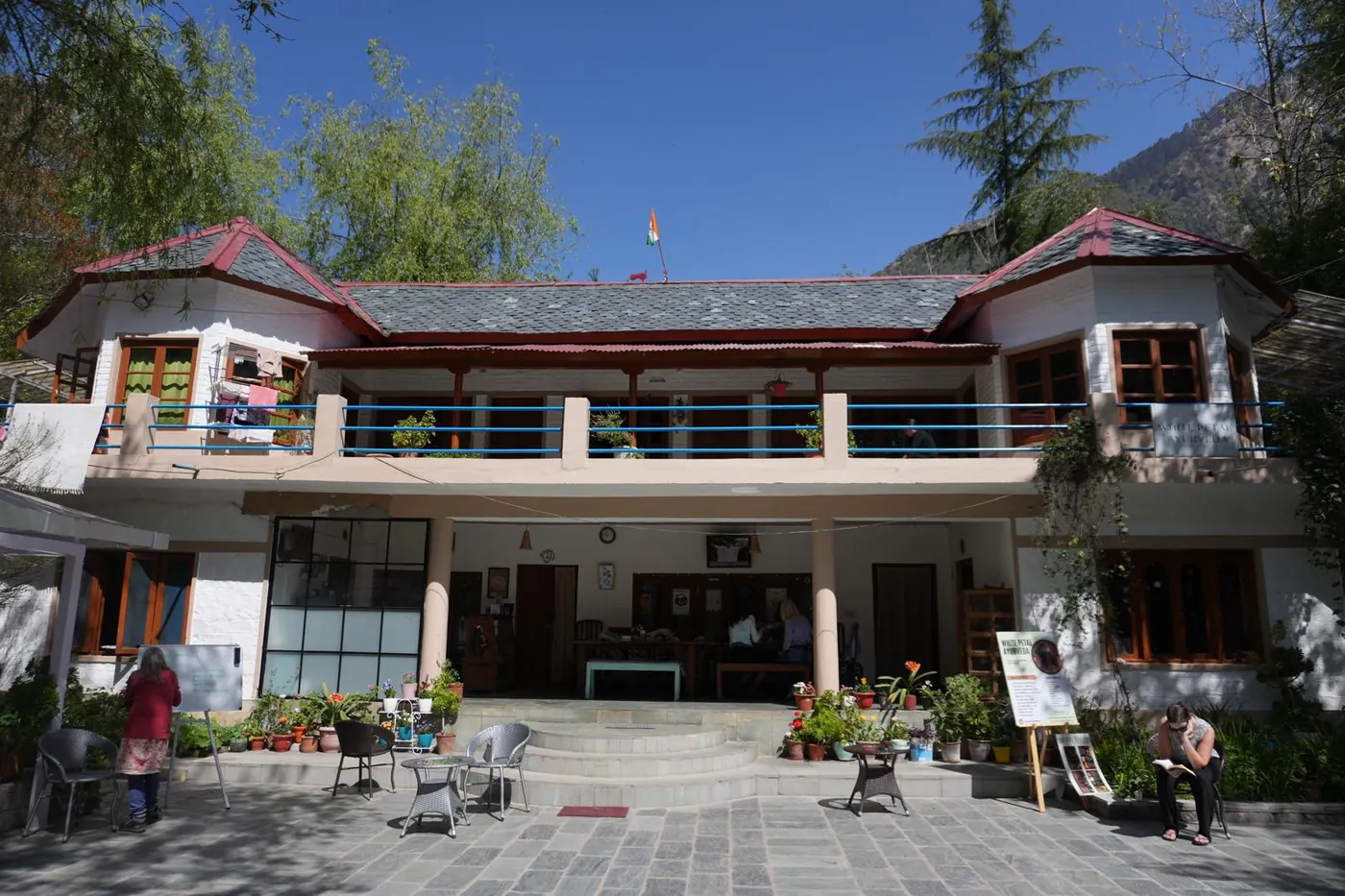 Exterior courtyard of the Trimurti retreat centre beneath Himalayan trees and mountains.