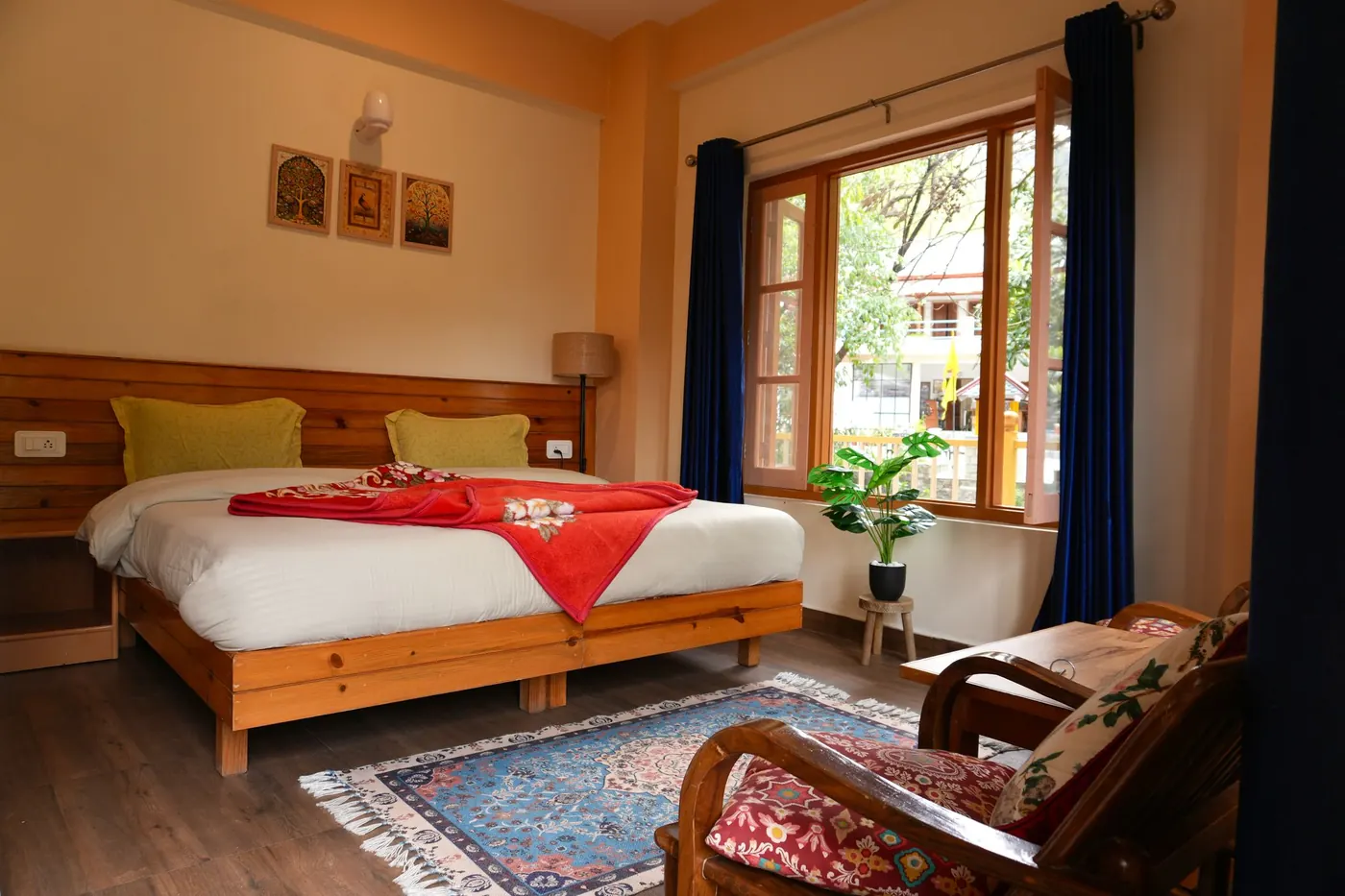 Guest room at Trimurti with a wooden bed, red accents, and a window overlooking the grounds.